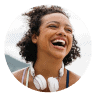 Smiling woman with curly hair and white headphones around her neck, set against a circular coral background. Represents joy, energy, and the supportive Noom community.