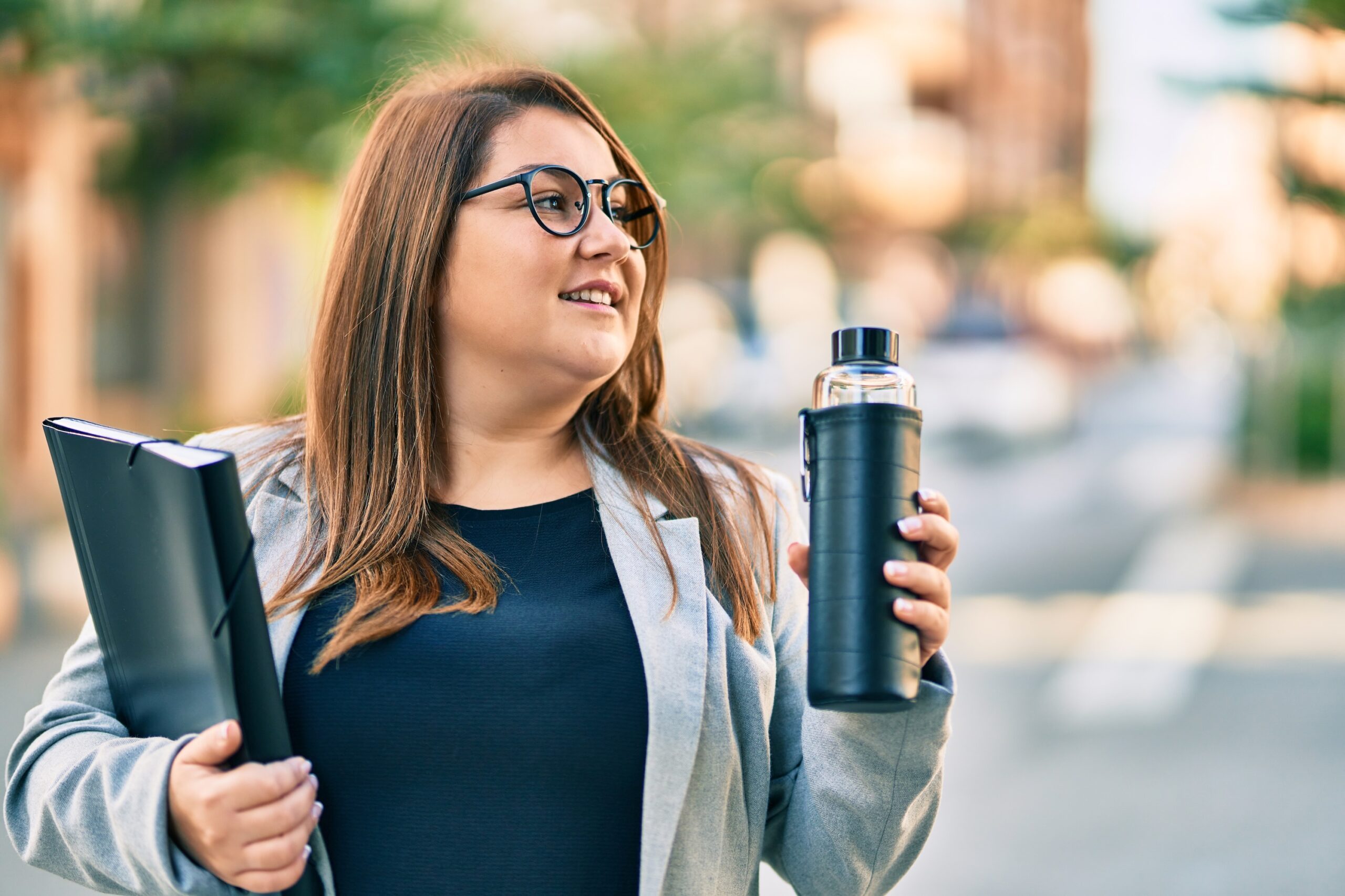 Young plus size businesswoman holding binder and bottle of water at the city. Photography, Face, Head